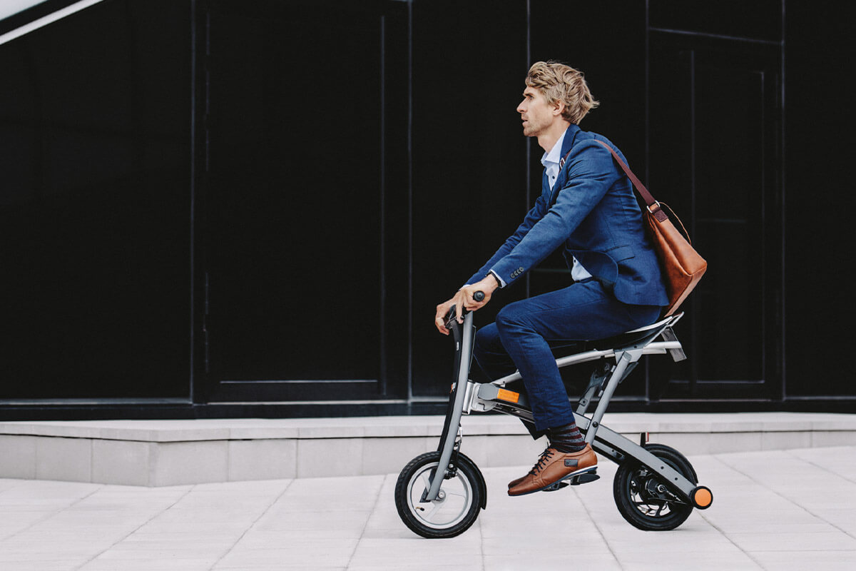 Man riding electric bike Stigo in business suit near modern office building.
