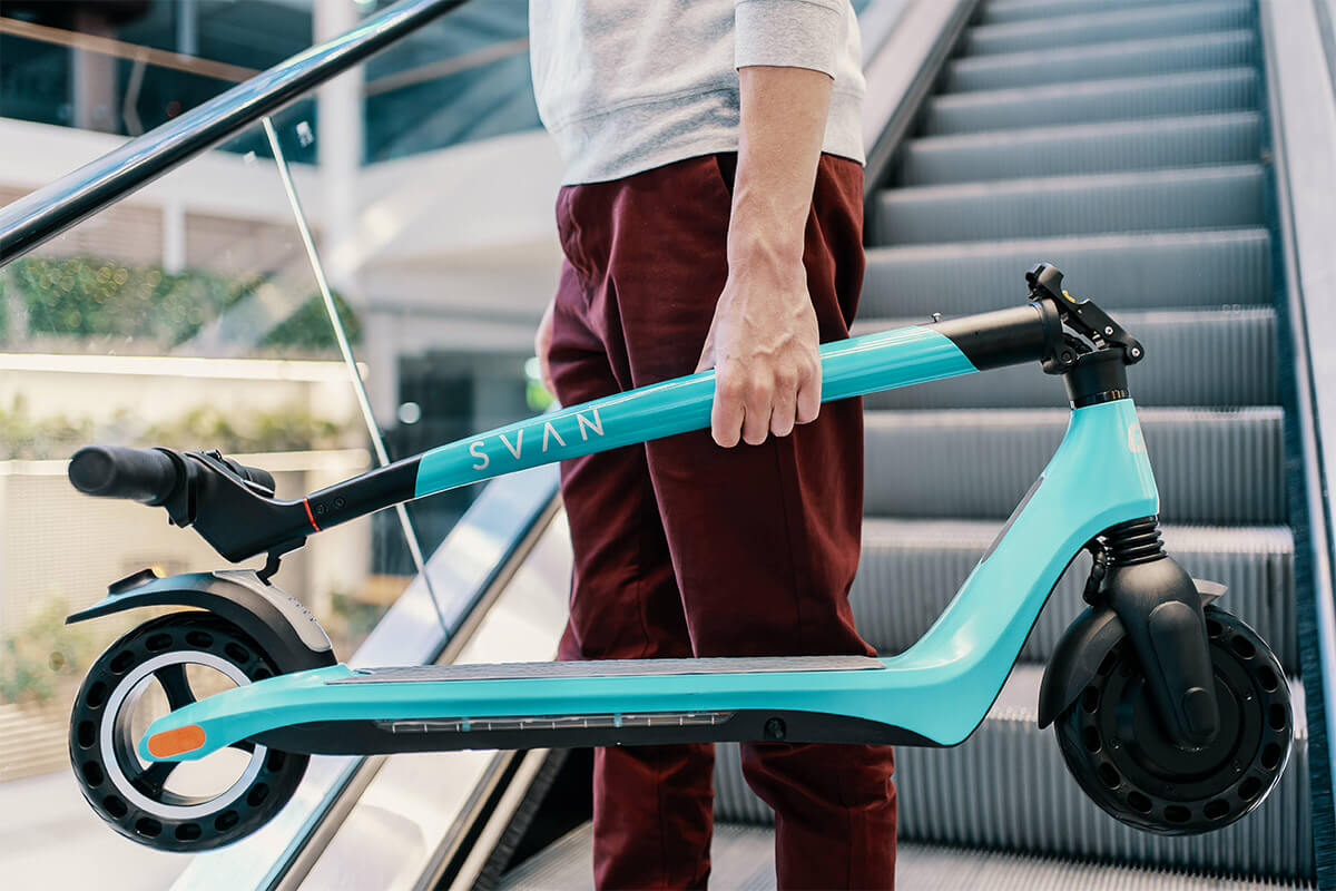 Image of a man in front of escalator carrying a green folded Electric scooter Gpad Svan Max