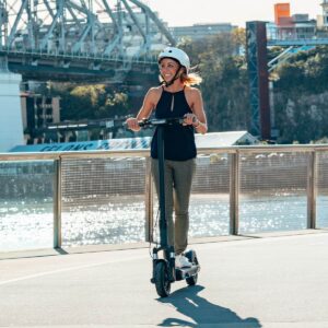 Image of a woman riding Electric scooter inmotion s1 at the pier and a port in in the background.
