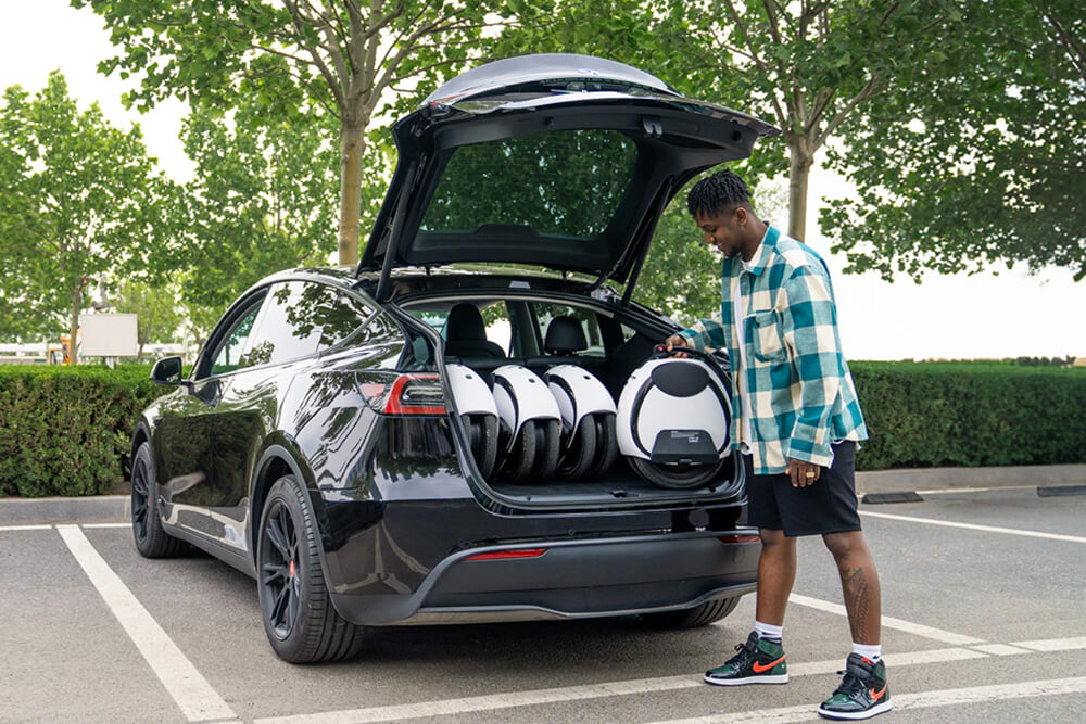 Person loading the Inmotion E20 electric unicycles into the trunk of a black car parked outdoors, demonstrating easy transport and storage.