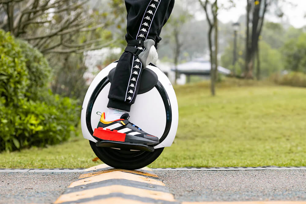 Close-up of a person riding the Inmotion E20 electric unicycle over a speed bump in a park, highlighting the vehicle’s balance and agility.