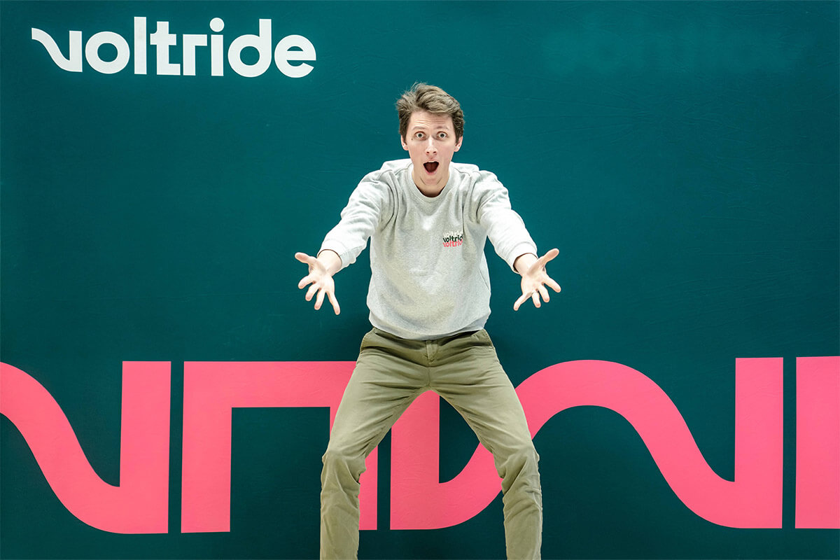 Enthusiastic man posing playfully in front of a colorful Voltride backdrop, arms outstretched and expression full of excitement.