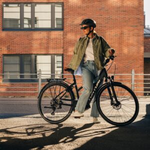 Side view of a woman standing with a Tunturi eMotion electric bicycle on the city street wearing a helmet.
