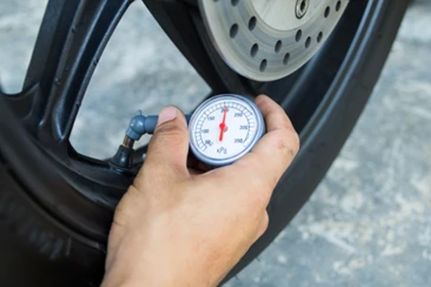 A persons hand holds a tire pressure gauge against the valve of a wheel to check air pressure.